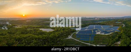 Panoramablick aus der Vogelperspektive auf den Sonnenuntergang am Horizont und auf einem Hügel auf einer Solarfarm Stockfoto