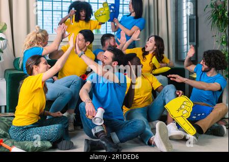 - JA, ICH WEISS Multiethnische Sportfans, die lachen, fünf geben, schreien und die Faust abpumpen, um das Tor der Lieblingsfußballmannschaft zu feiern. Glückliche Leute, die j trinken Stockfoto