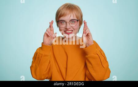 Aufgeregte blonde Frau drückte die Daumen, um in die Kamera zu schauen, um nach Glücksnachrichten zu fragen, wünschte gute Prüfungsergebnisse, träumte vom Sieg im Lotto-Jackpot. Mädchen isoliert auf gelbem Studiohintergrund Stockfoto