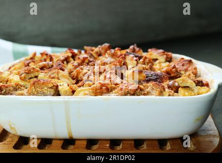 Frisch gebackene Bananen-Walnuss-Brotpudding in einer Keramikschale auf einem Holzbalken Stockfoto