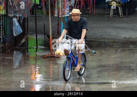 SAMUT PRAKAN, THAILAND, MAI 10 2023, Ein Mann, der auf einem Fahrrad in der Rainy Street fährt. Stockfoto