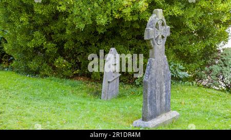 Ein antiker Grabstein in Form eines keltischen Kreuzes in der Nähe der Kathedrale Saint Fin Barre in Irland. Alte Steinkreuze auf einem Friedhof. Religiöse Ziele Stockfoto