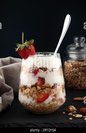Ein Glas Parfait aus Müsli, Beeren und Joghurt auf dem Tisch. Mit Erdbeeren dekoriert. Gesundes Frühstückszerealien. Stockfoto
