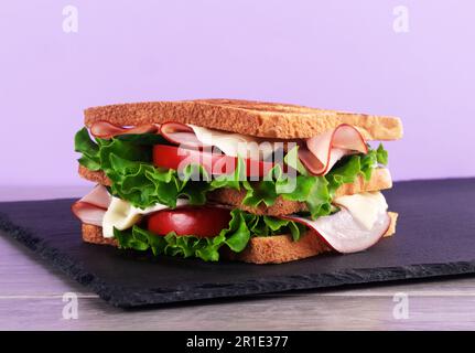 Köstliches Schinken-Sandwich mit frischem Salat und Gurke, serviert auf einem Steinbrett. Stockfoto