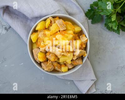 Fleischeintopf mit Kartoffeln und Karotten. Schweinefleisch, gedünstet mit Gemüse auf grauem Hintergrund mit grauem Leinentuch und Petersilie. Lecker und nahrhaft Stockfoto