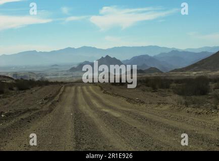 Eine verlassene Schotterstraße, die zu den zerklüfteten blauen Bergen führt Stockfoto