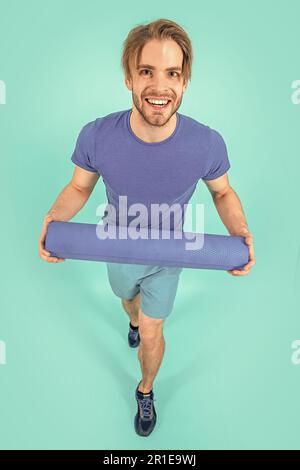 Glücklicher Sportler mit Yogamatte im Studio. Foto eines Sportlers mit Yogamatte. Sportler mit Yogamatte in Sportbekleidung. Sportmann mit Yogamatte Isolate Stockfoto