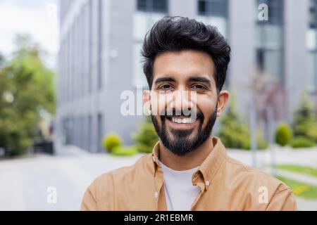 Nahaufnahme Foto eines jungen Hindu-Studenten, lächelnder Mann, der in die Kamera schaut, Geschäftsmann außerhalb des Bürogebäudes, der ein Hemd trägt. Stockfoto