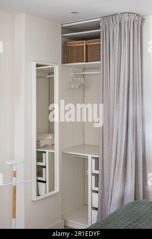Vertikaler Schuss komfortabler Ankleideraum mit grauem Vorhang und Stauraum für Sachen und Kleidung im Schlafzimmer. Kompaktes, aber funktionelles Konzept Stockfoto