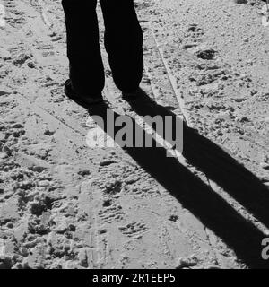 Person, die auf hellem Schnee steht und einen langen Schatten wirft Stockfoto