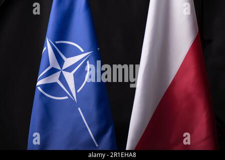 Ukraine, Kiew - 10.04.2023. Offizielle Flaggen Polens und der NATO vor schwarzem Hintergrund. Ein Symbol der Einheit und Widerstandsfähigkeit in einer Welt der Unsicherheit und Stockfoto