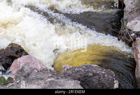 Stromschnellen. Nahaufnahme des abstrakten Hintergrunds von fallendem Wasser. Das Wasser fließt über die Felsen des Flusses. Ein wunderschöner, mächtiger Fluss eines stürmischen Bergflusses. Die Stockfoto