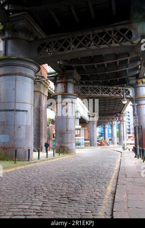 Fußgängerblick auf eine Steinstraße unter einer alten Metallbrücke Stockfoto