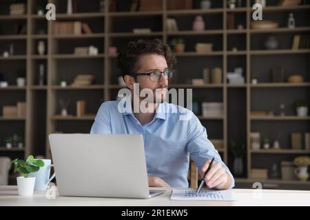 Aufmerksamer, seriöser junger Geschäftsmann mit Brille, der mit einem Laptop arbeitet Stockfoto