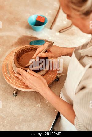 Ich benutze Ton, um Kunstwerke zu erschaffen, eine Frau, die in ihrer Werkstatt einen Tontopf formt. Stockfoto