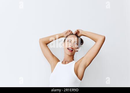 Eine Frau mit gebräunter Haut, die Musik hört und mit den Händen in den kabellosen Kopfhörern tanzt und mit ihren Zähnen vor einem weißen Gesicht lächelt Stockfoto