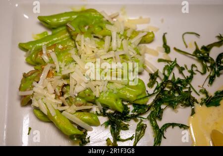 Italienische Küche, frische hausgemachte Pasta aus grünem Brokkoli und Penne mit Parmesan Parmigiano reggiano Käse Sauce mit getrocknetem Rucolasalat auf weißem Eber Stockfoto