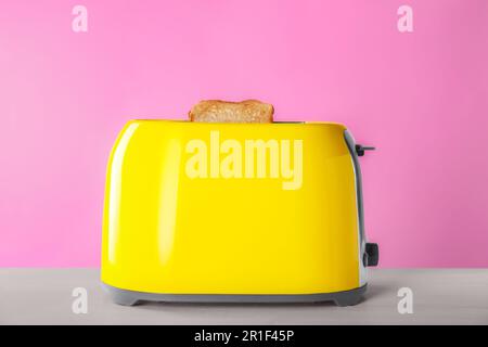 Moderner Toaster mit Scheiben gebratenes Brot auf einem weißen Holztisch Stockfoto