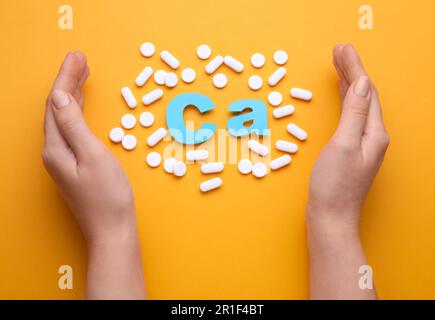 Frau mit Pillen und Kalzium-Symbol aus hellblauen Buchstaben auf orangefarbenem Hintergrund, Draufsicht Stockfoto