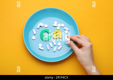 Frau, Teller mit Pillen und Kalziumsymbol aus bunten Buchstaben auf orangefarbenem Hintergrund, Draufsicht Stockfoto