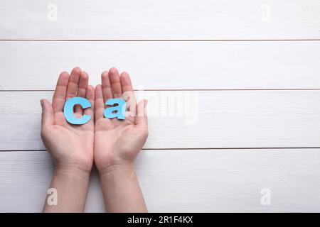 Frau, die das Papiersymbol Ca (Calcium) auf dem weißen Holztisch hält, Draufsicht Stockfoto