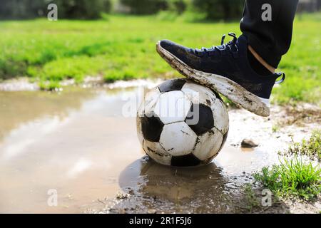 Mann mit schmutzigem Fußball in der Nähe der Pfütze draußen, Nahaufnahme Stockfoto