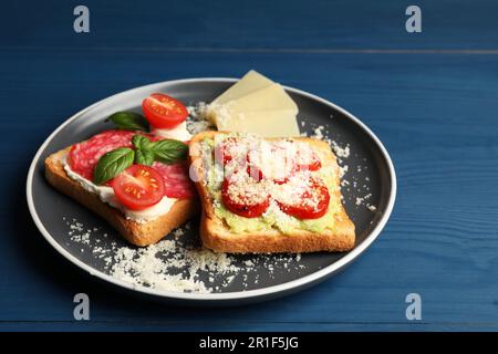 Leckere Toasts mit verschiedenen Belägen, serviert auf einem blauen Holztisch Stockfoto