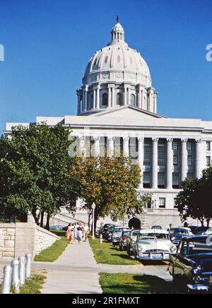 Autos, die an einer Straße vor dem Kapitol des Bundesstaats Missouri in Jefferson City, Missouri, geparkt werden. Eine Gruppe von Frauen und Männern, die auf dem Bürgersteig vom Kapitolgebäude (r) ca. 1950-1955 Stockfoto