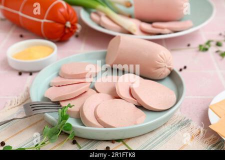 Zusammensetzung mit gekochter Wurst auf dem Teller, grünen Zwiebeln und Sauce auf einem rosa Fliesentisch Stockfoto