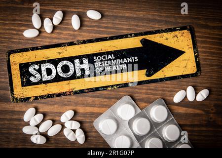 SDOH Soziale Determinanten der Gesundheit. Gelbes Richtungsschild mit Text und Pillen auf Holzhintergrund. Stockfoto