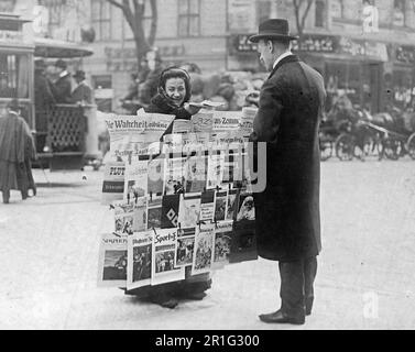 Archivfoto: Eine Frau, die Zeitungen verkauft, ein Mann, der eine Zeitung an einer Straßenecke in Deutschland kauft. 1908-1919 Stockfoto