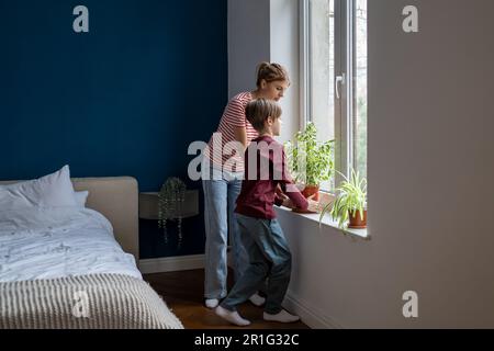 Aufmerksamer Sohn Junge, der Hausarbeiten macht, mit mutter, die sich um grüne Pflanzen kümmert. Zeit für die Familie. Stockfoto