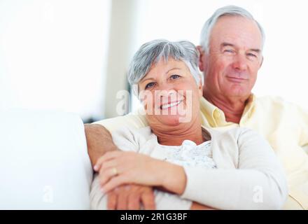 Lächelndes, reifes Paar, das sich auf der Couch entspannt. Porträtliebes reifes Paar, das sich auf einer bequemen Couch entspannt. Stockfoto
