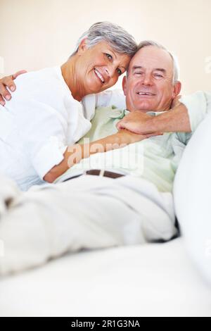 Liebevolles, reifes Paar, das sich zu Hause entspannt. Porträt eines liebevollen, erwachsenen Paares, das lächelt, während es sich auf der Couch entspannt. Stockfoto