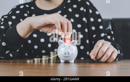 Die Hand einer Geschäftsfrau, die eine Münze hält und die Lohnerhöhung mit weißem Pfeil einsetzt, um Geld zu sparen, wächst auf einem Haufen Geld. Investieren Sie Futu Stockfoto