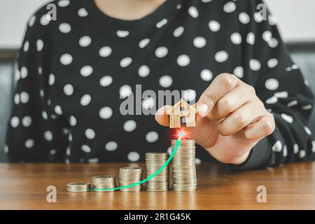 Die Hand einer Geschäftsfrau, die eine Münze in der Hand hält, mit weißem Pfeil, wächst auf einem Haufen Geld. Investieren Sie Zukunft, Kredit, Finanzen, in Stockfoto