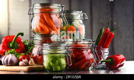 Gläser mit mariniertem Essen und rohes Gemüse auf Schneidebrett Stockfoto