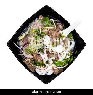 Blick von oben auf vietnamesische Suppe Pho Bo mit Reisnudeln, Brühe, Zwiebeln, Gemüse, Rindfleisch in der Schüssel mit Ausschnitt aus Keramiklöffel auf weißem Hintergrund Stockfoto