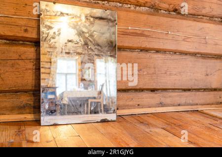 Alter Spiegel steht auf Holzboden im ländlichen Holzhaus (Fokus auf Spiegel) Stockfoto