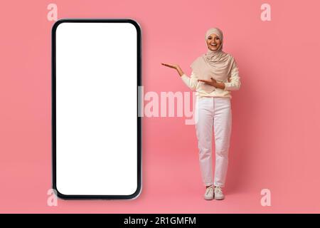 Wunderschöne Muslimische Frau In Hijab Präsentiert Großes Smartphone Mit Weißem Bildschirm Stockfoto