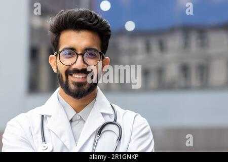 Nahaufnahme eines hinduistischen Arztes, Mann mit Brille, der lächelt und in die Kamera schaut, Praktikant mit Stethoskop außerhalb der Klinik. Stockfoto