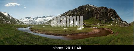 Panoramablick auf das Pyrenäische Tal, ein Fluss aus kristallklarem Wasser, der ein Tal durchquert, umgeben von felsigen Gipfeln im Vordergrund und Schnee Stockfoto