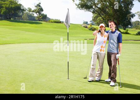 Ein Golfpaar, das auf dem Putting Green steht. Ein langes Golfpaar, das auf dem Putting-Green steht und Arme umgibt. Stockfoto