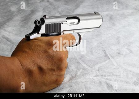 Rechte Hände halten kompakte halbautomatische Geschützpakete, die auf das Ziel zielen, isoliert auf einer weißen Schürze. Stockfoto