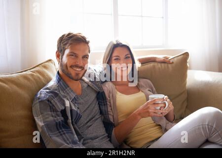 Porträt, Kaffee und Paare entspannen oder lächeln auf einer Couch zusammen oder sich im Wohnzimmer und mit Tee verbinden. Mann, Frau und Liebe oder Zuneigung mit Hitze Stockfoto