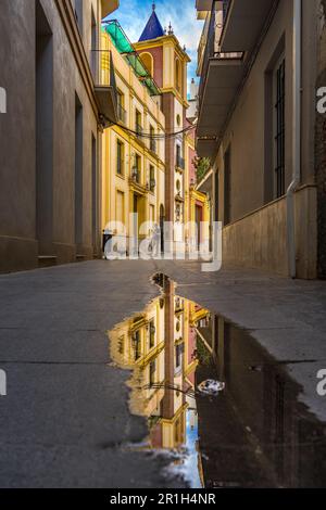 Málaga, Spanien - Nov. 25 2022: Altstadt von Málaga mit dem Turm der Kathedrale im Hintergrund, reflektiert in einer Pfütze Stockfoto