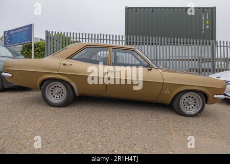Rayleigh, Großbritannien. Mai 2023. Eine klassische, viertürige Vauxhall Victor Limousine mit Chromdetails steht auf Kies vor einem grünen Versandcontainer und einem Metallzaun in Rayleigh, Essex. Der Oldtimer steht im Kontrast zur industriellen Kulisse und erinnert an Themen wie Nostalgie und städtische Transformation. Farm Fresh Garage Truck und amerikanische Fahrzeuge werden gezeigt. Penelope Barritt/Alamy Live News Stockfoto