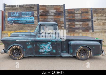 Rayleigh, Großbritannien. Mai 2023. Ein verwitterter Pickup-Truck im Stil 1956 mit türkisfarbenen Akzenten und Goodyear-Reifen, der vor einer Beton- und Holzwand an einer lizenzierten Müllverladestation in Rayleigh, Essex, geparkt wird. Die Szene stellt klassische Automobilkultur und städtische industrielle Infrastruktur gegenüber. Farm Fresh Garage Truck und amerikanische Fahrzeuge werden gezeigt. Penelope Barritt/Alamy Live News Stockfoto
