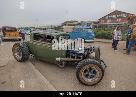 Rayleigh, Großbritannien. Mai 2023. Ein mattgrüner Vintage Hot Rod mit freiliegendem Motor und übergroßen Hinterreifen parkt in Rayleigh während einer öffentlichen Autoausstellung. Die Szene umfasst einen blauen VW-Van Typ 2, einen kastanienbraunen Kombi und Fußgänger, die die Veranstaltung erkunden. Farm Fresh Garage Truck und amerikanische Fahrzeuge werden gezeigt. Penelope Barritt/Alamy Live News Stockfoto
