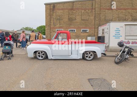 Rayleigh, Großbritannien. Mai 2023. Ein rot-weißer Vintage-Pickup mit abgesenkter Federung und kundenspezifischen Rädern steht neben einem Imbissstand, der Tee, Kaffee, Kuchen und Chips anbietet. Ein Motorrad und mehrere Fußgänger, darunter eine Person, die einen Kinderwagen schiebt, deuten auf eine lebhafte öffentliche Veranstaltung in Rayleigh, Essex, hin. Farm Fresh Garage Truck und amerikanische Fahrzeuge werden gezeigt. Penelope Barritt/Alamy Live News Stockfoto